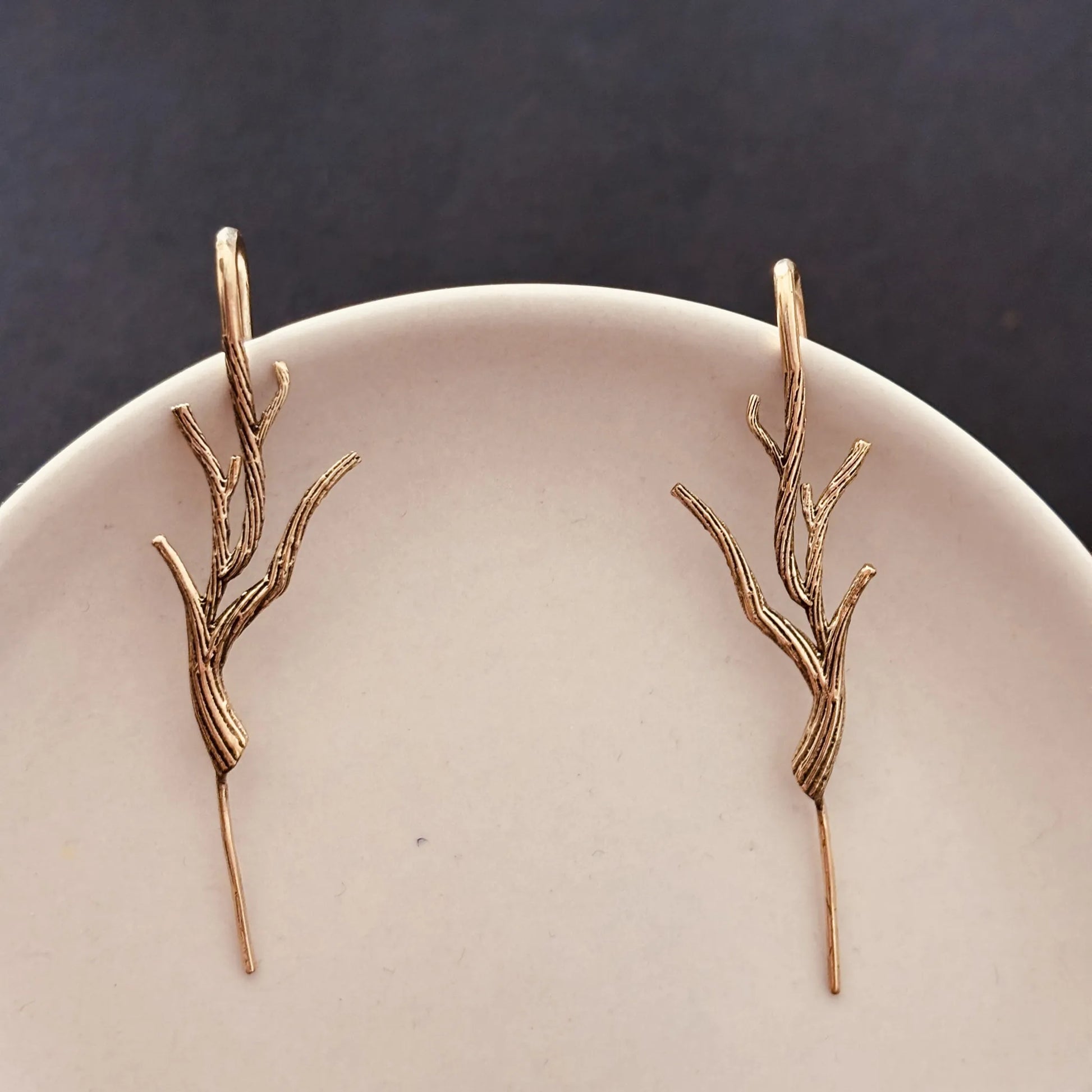 Brass Barebranch earrings resting on minimal white plate against dark backdrop