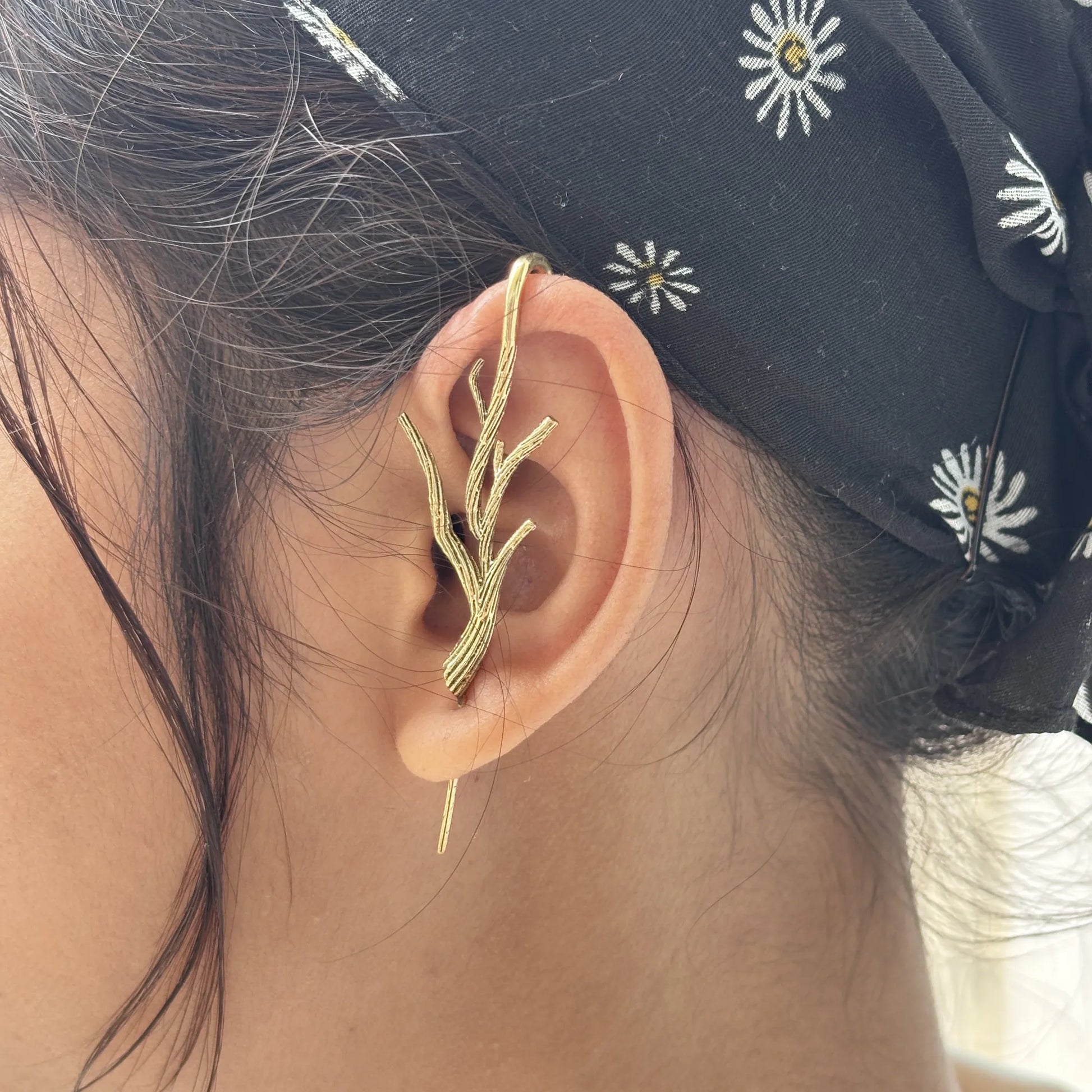 Brass branch-shaped earrings worn on ear, styled with black floral headscarf