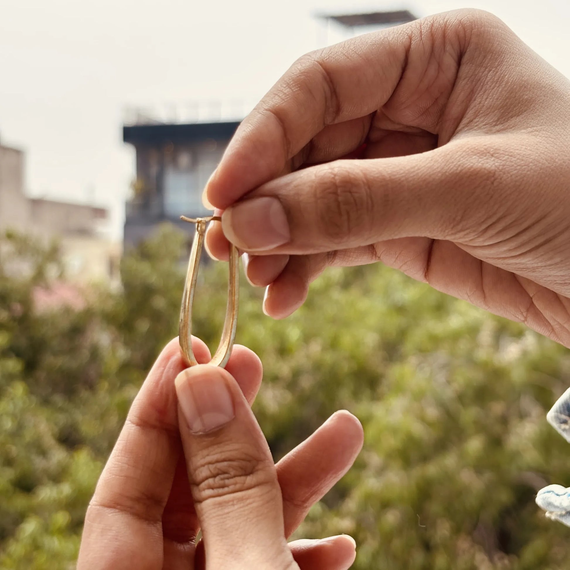 Elongated brass hoops held gently in hand, outdoors