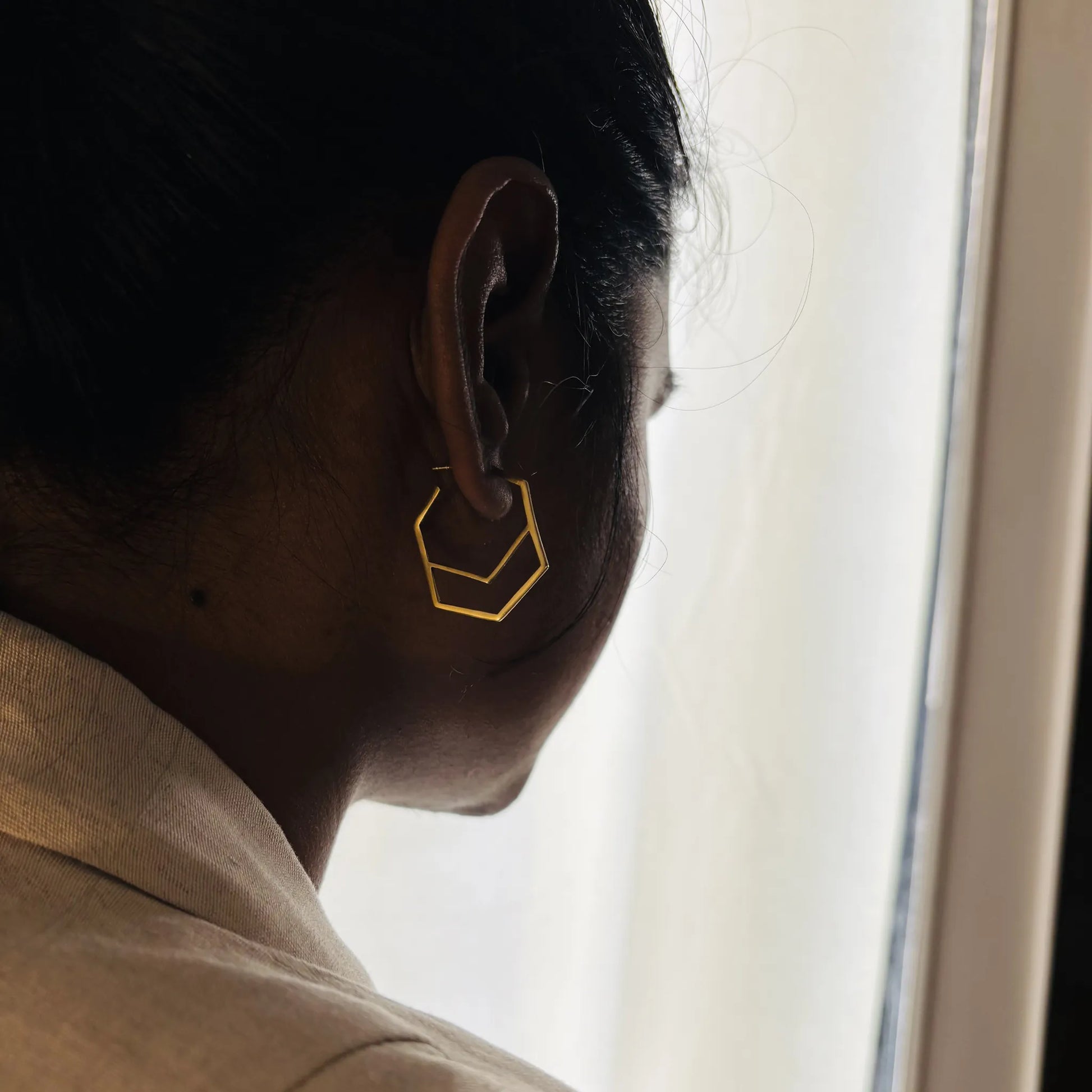 Geometric brass hoop earrings worn on ear, profile view in soft natural light