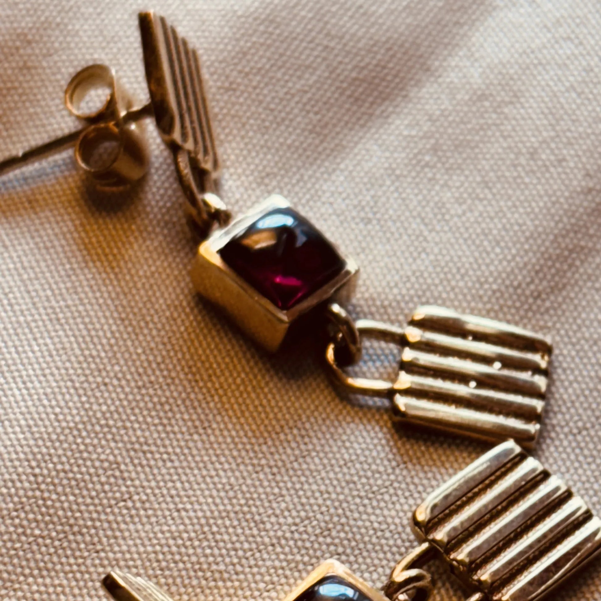 Close-up of garnet brass earrings showing textured metal and square stone