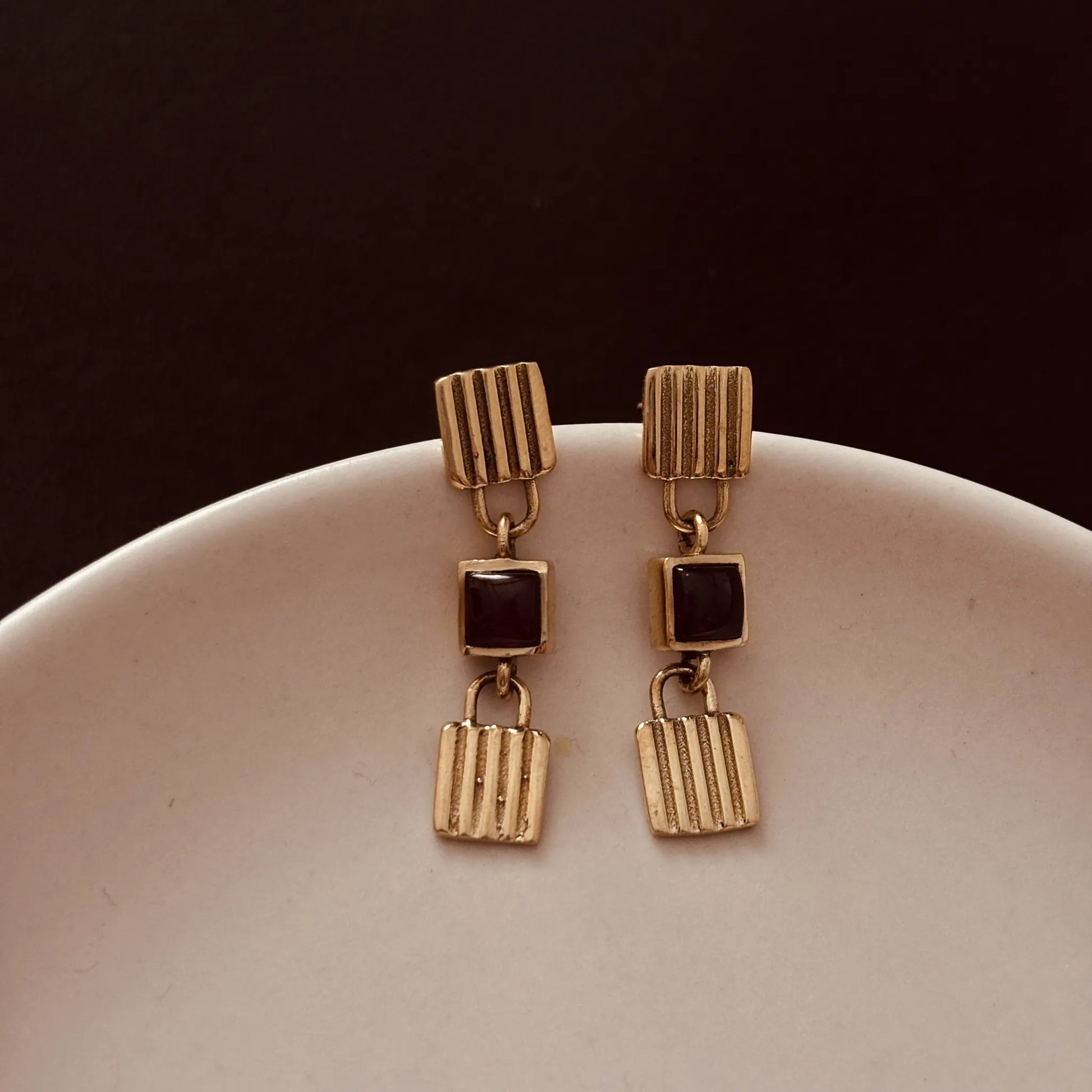 Garnet brass earrings placed on a ceramic plate with dark background