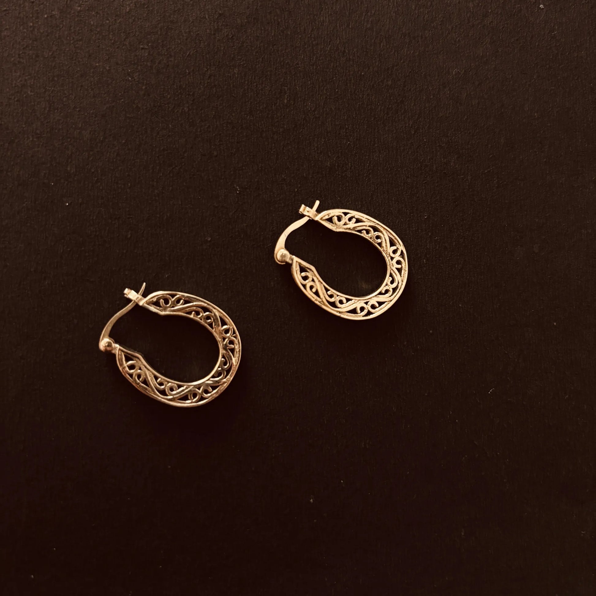 Vintage-inspired etched brass hoops on a dark background