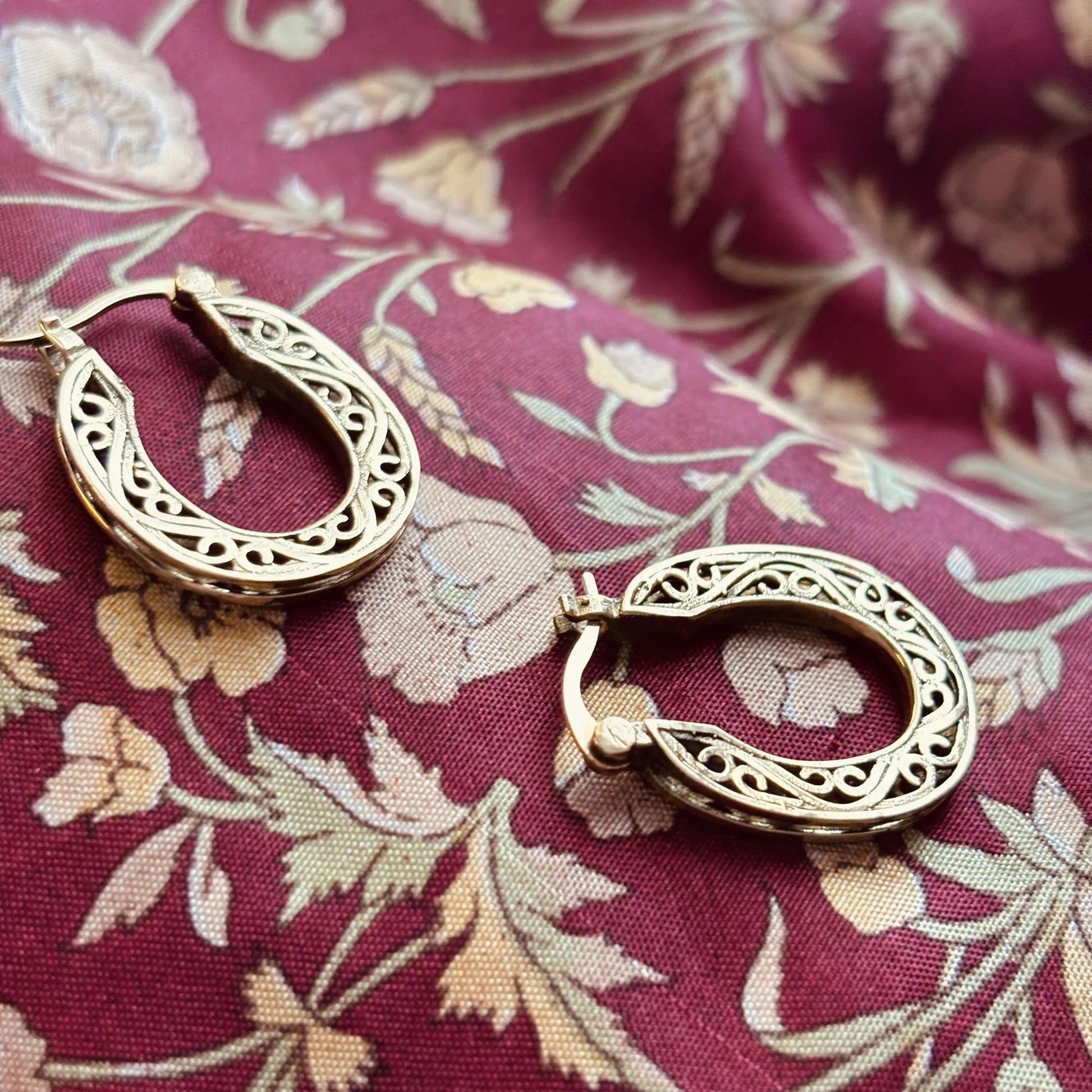 Intricately designed brass hoops resting on maroon floral fabric