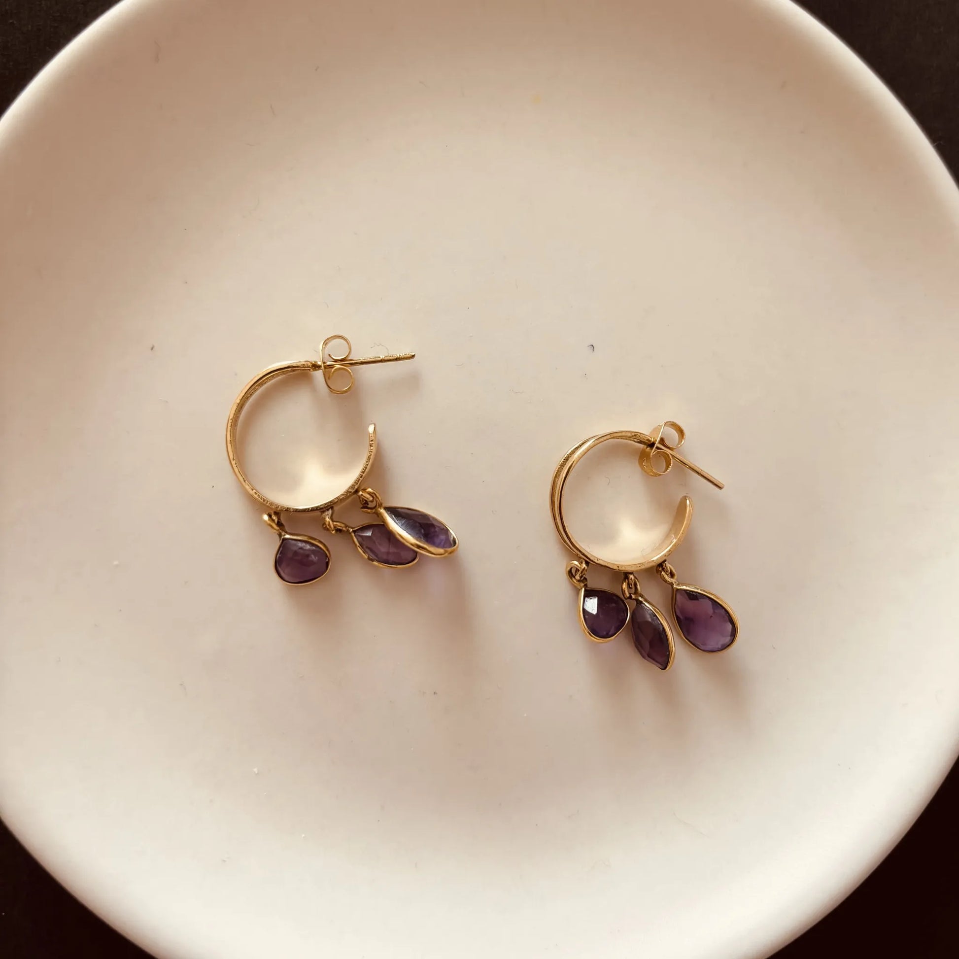 Pair of brass amethyst hoop earrings placed on a ceramic plate