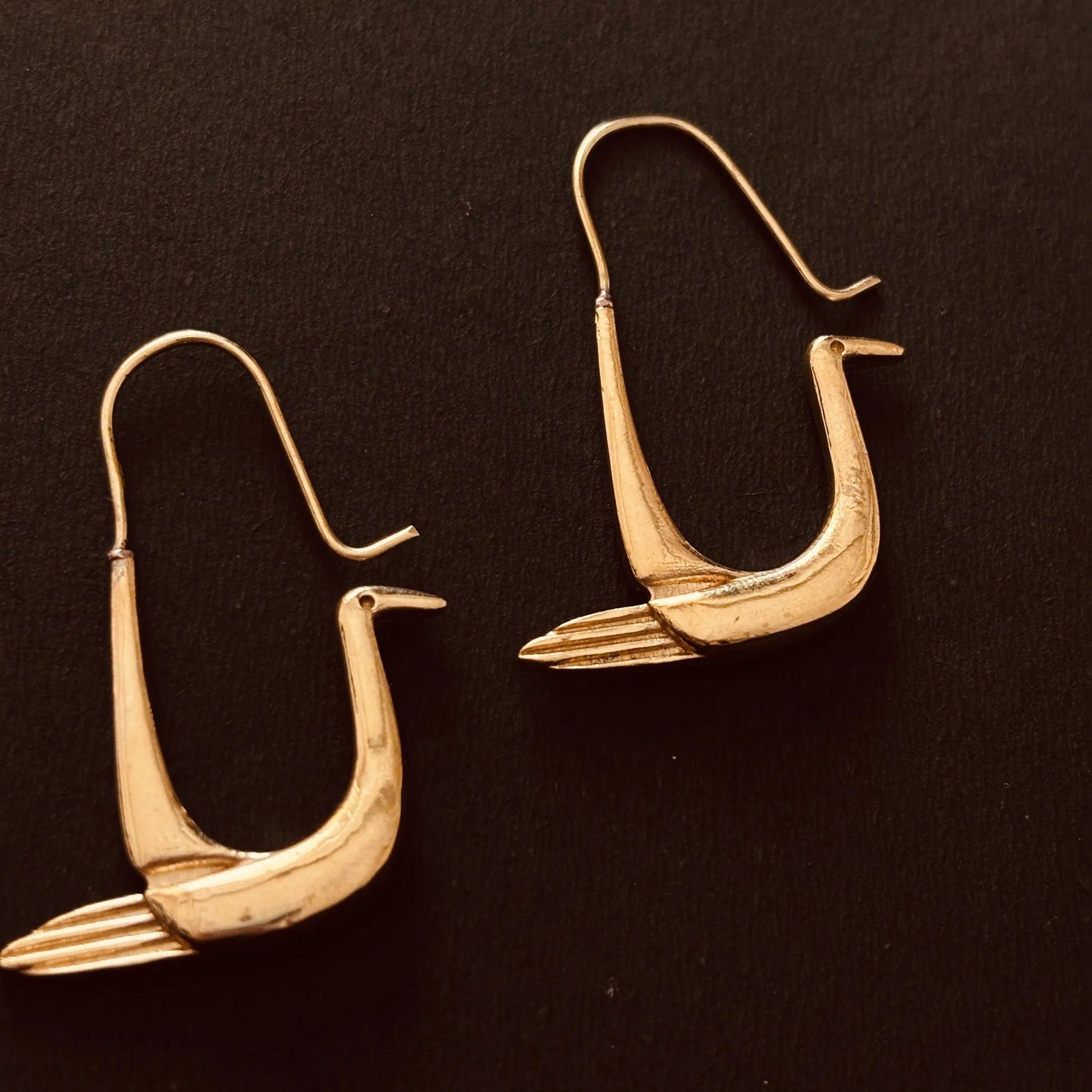 Pair of Soaring Still brass earrings laid flat on black background