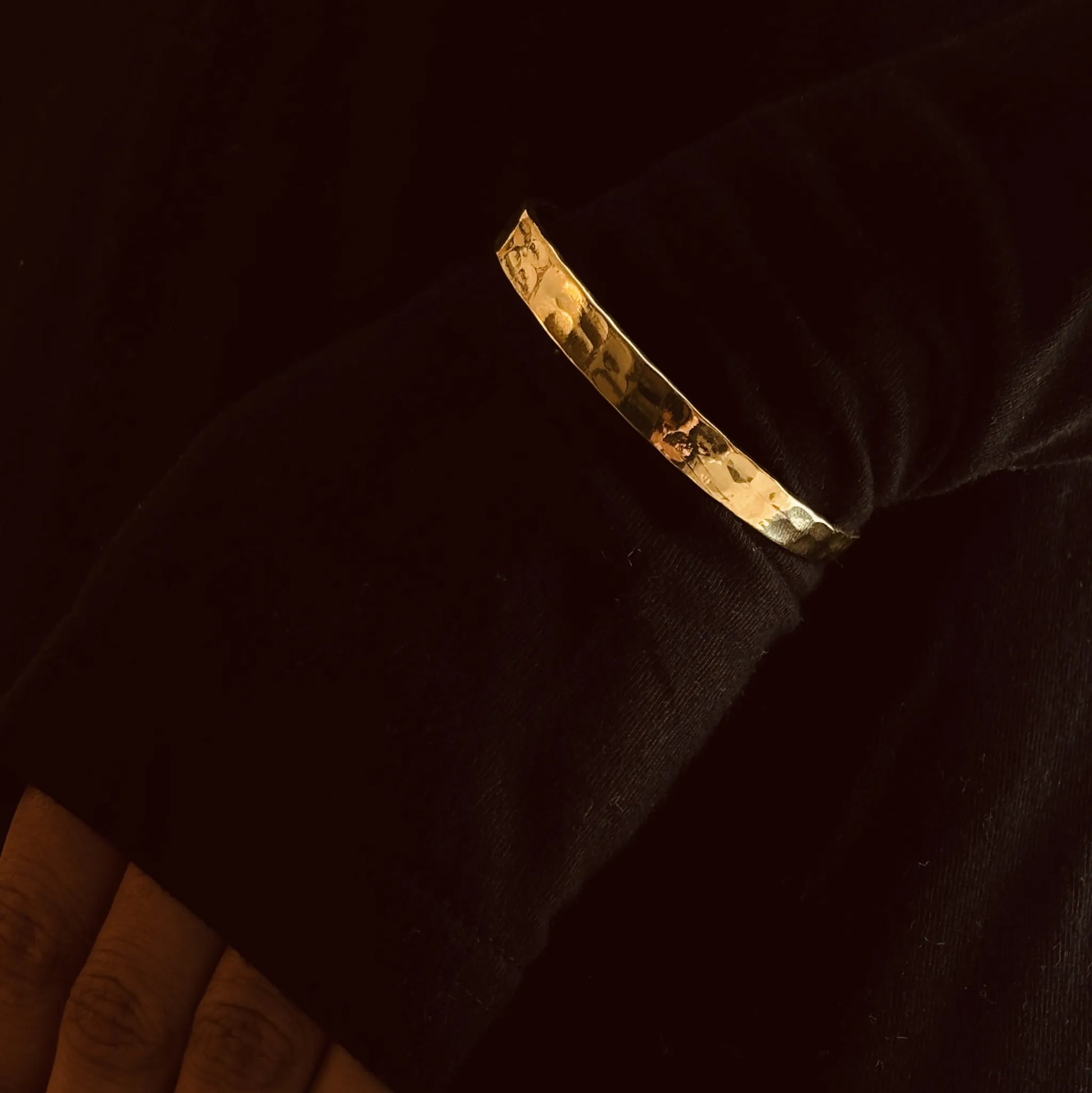 Brass cuff bracelet over black sleeve, arms folded softly