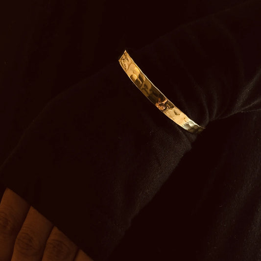 Brass cuff bracelet over black sleeve, arms folded softly