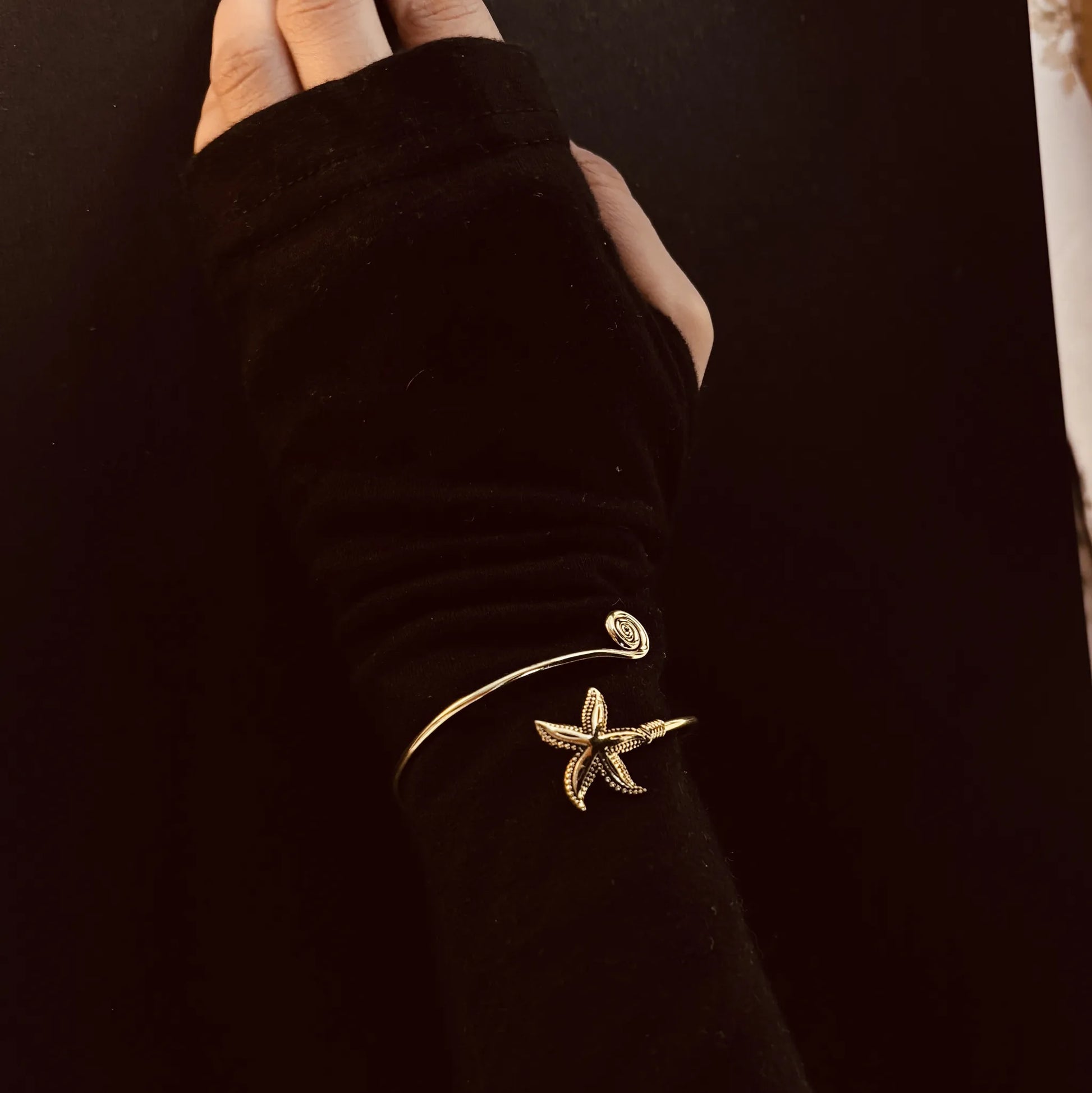 Brass starfish cuff styled over black long-sleeve arm against dark background