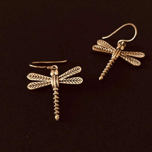 Dragonfly-shaped brass earrings placed flat on black background