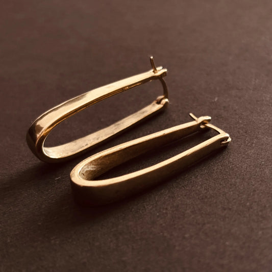 Sculptural elongated brass hoops placed on dark surface
