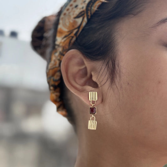 Garnet brass drop earrings worn on ear, styled with patterned headscarf