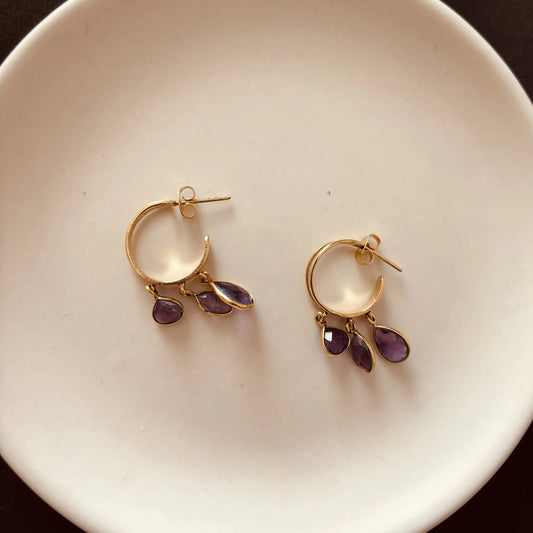 Pair of brass amethyst hoop earrings placed on a ceramic plate