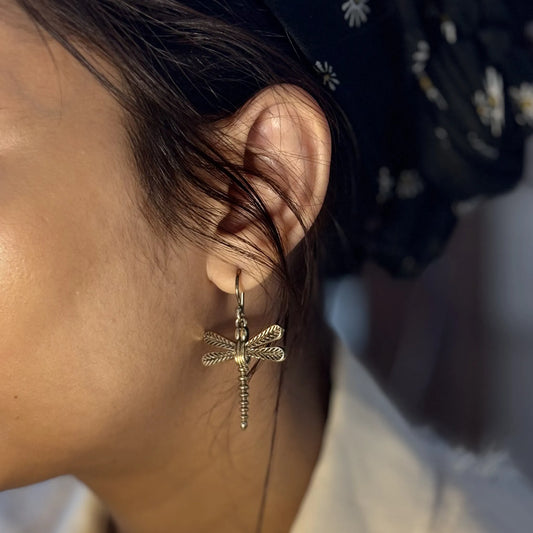 Brass dragonfly earrings worn on ear, styled with black floral headscarf